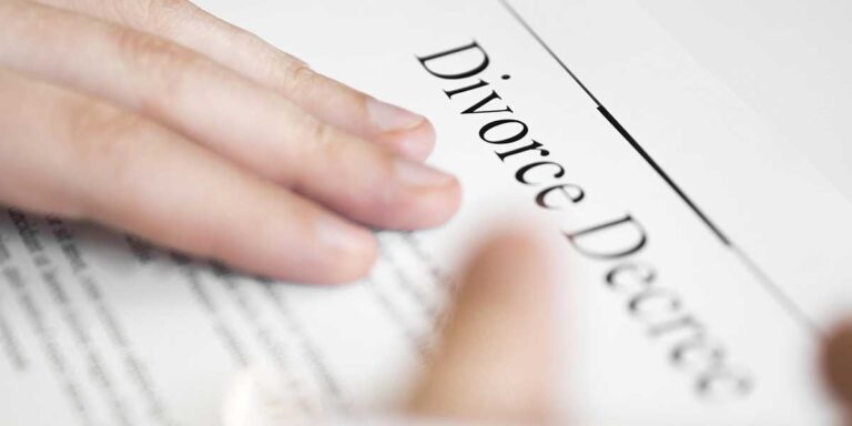 A close-up view of a hand resting on an official document clearly titled Divorce Decree placed on a table.