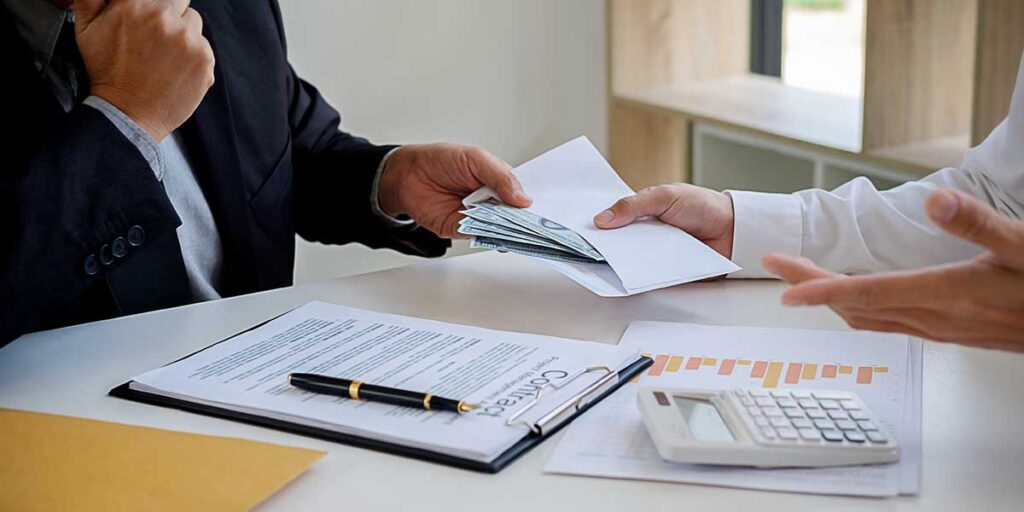 An estate executor hands cash in an envelope to a professional reviewing legal documents regarding probate creditor claims.