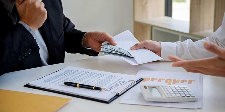 An estate executor hands cash in an envelope to a professional reviewing legal documents regarding probate creditor claims.