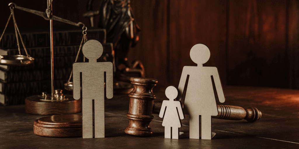 Wooden family figures standing next to a gavel and scales of justice, representing the legal burden of proof